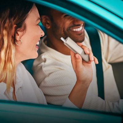 A woman in a car hoding an IQOS ILUMA ONE device. 
