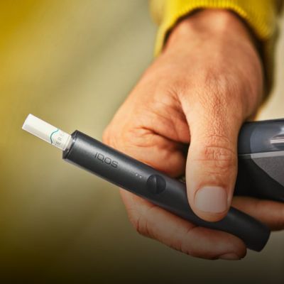 A hand holding an IQOS ILUMA device with a TEREA tobacco stick inserted.