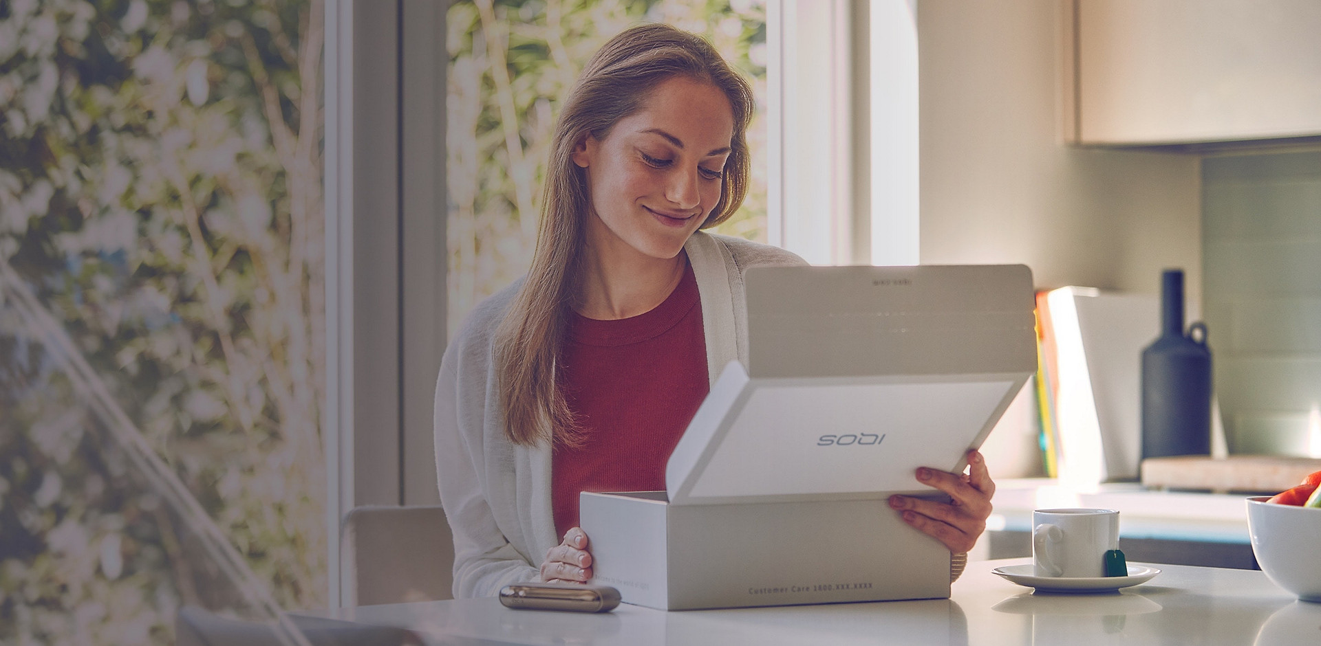 A woman smiling as she looks into the packaging box her IQOS ILUMA device came in