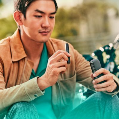 جهاز IQOS بين يدين أمام عجلة قيادة السيارة.