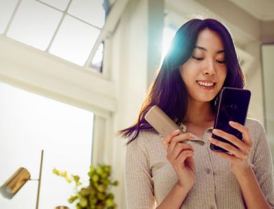 Una mujer usa el dispositivo IQOS ILUMA mientras escribe un mensaje de texto en su celular