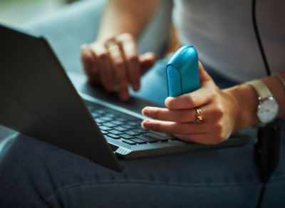 A person conducts an online diagnostic on a blue IQOS ILUMA pocket charger