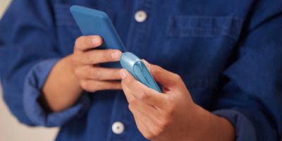 Ein Mann mit einem IQOS Originals Dup und einem Smartphone in den Händen.