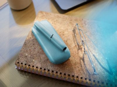 Dispositivo IQOS Originals Duo turquesa sobre una libreta junto a unos lentes