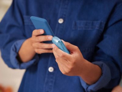 Homme tenant dans une main l'appareil IQOS Originals Duo en turquoise et dans l'autre un téléphone portable.