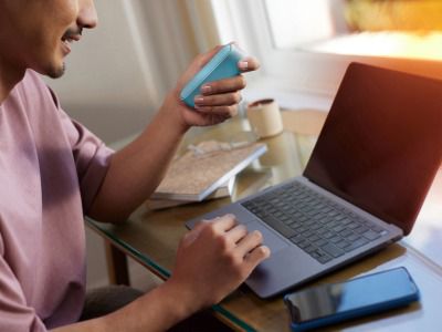 Hombre sosteniendo un dispositivo IQOS Originals Duo y escribiendo en una laptop