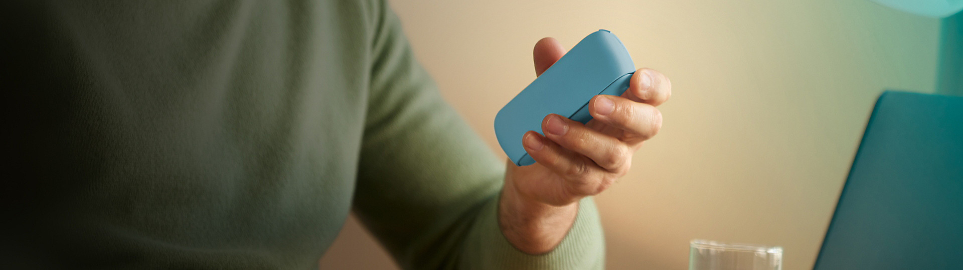 A close-up of a person wearing a green jersey holding an IQOS ILUMA holder in their hand