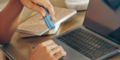 Frauenhänd die ein IQOS Originals One nutzen währen an einem Laptop gearbeitet wird.