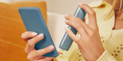 Eine Frau hält ein Smartphone und ein IQOS Originals One in ihren Händen.