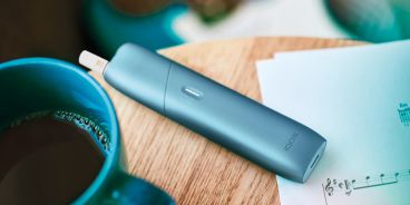 Kaffetisch mit verschiedenen Dokumenten und einem IQOS Originals One Gerät.