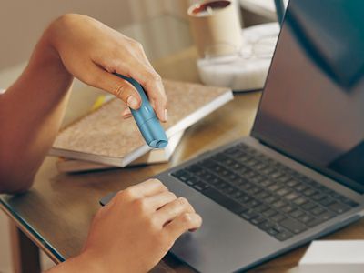 Eine Person sitzt am Laptop mit einem IQOS One in der Hand