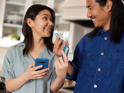 Hands holding a mobile phone and IQOS Originals One device, downloading the app to get the most of the heated tobacco device.