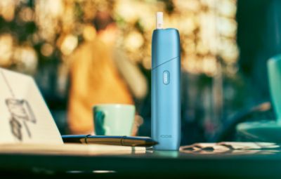 IQOS ORIGINALS ONE on a coffee table, in turquoise color.