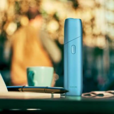 Appareil IQOS Originals ONE en turquoise à côté d'une tasse à café.