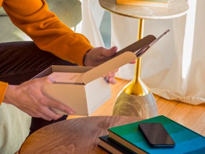 Mains tenant la boîte de l'appareil IQOS Originals Duo en turquoise.