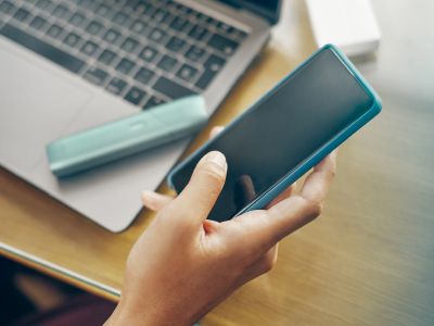 Femme tenant dans une main un téléphone, et l'appareil IQOS Originals One sur un ordinateur portable.