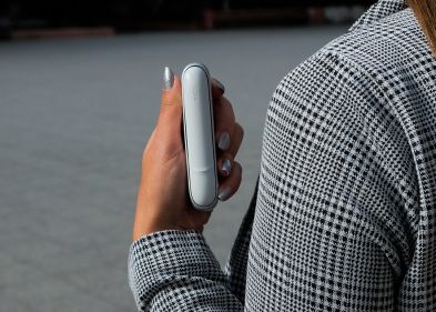 Person im karierten Blazer hält ein IQOS ORIGINALS DUO Silver im Freien.
