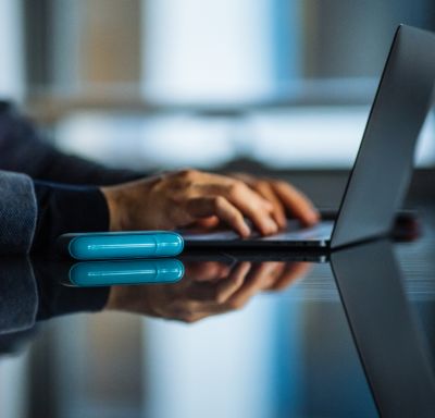 Ein blaues IQOS ORIGINALS DUO liegt neben einem Laptop auf einem Tisch.