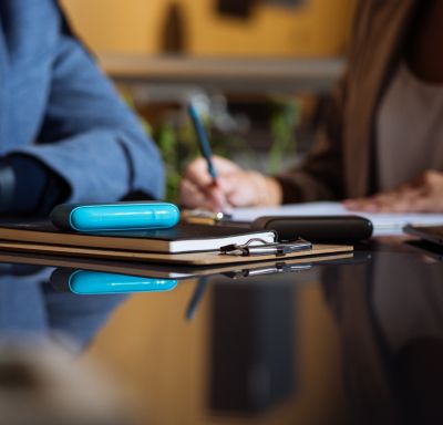 Ein blaues IQOS ORIGINALS DUO liegt auf einem Tisch zwischen Notizbüchern und Stiften.
