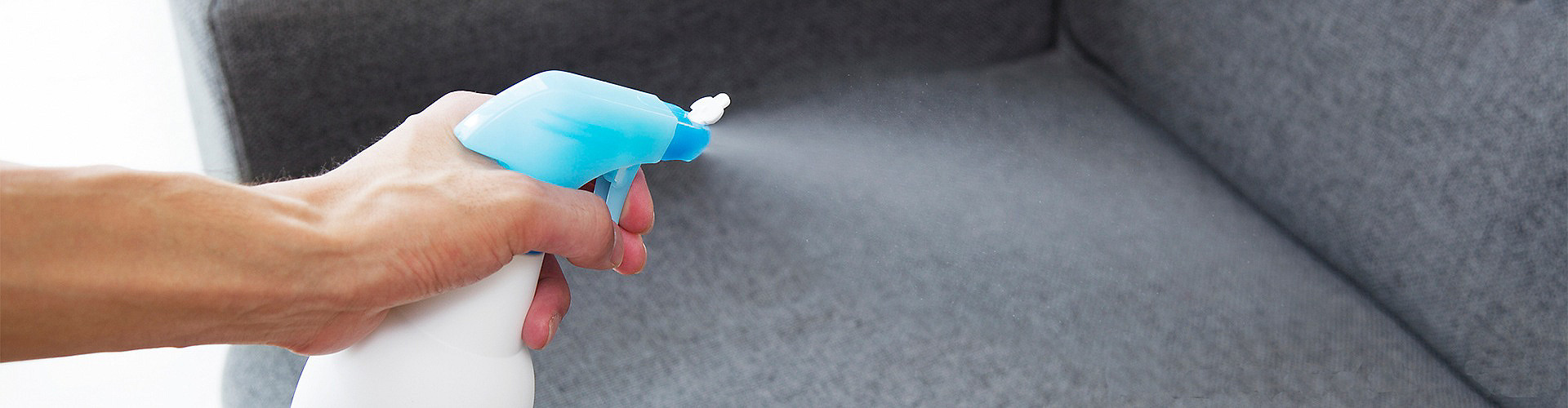Person cleaning sofa with spray to get rid of cigarette smell