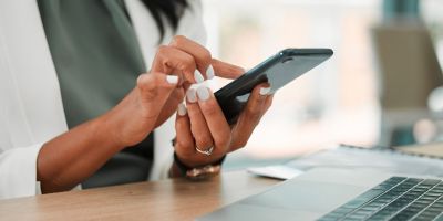 Mujer sentada a la mesa junto a su portafolios, con un teléfono, un pasaporte y un boleto de avión.