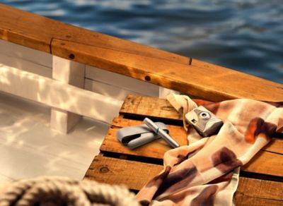 Türkiser IQOS-Charger mit Holder auf rustikalem Holztisch neben Sonnenbrille und Kamera.