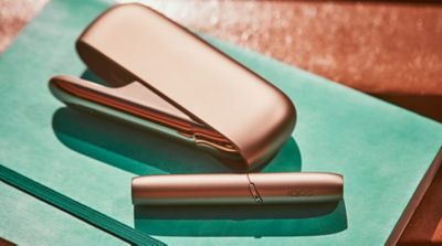 Gold IQOS DUO with a mobile, a glass of water and a yellow cup on a wooden table