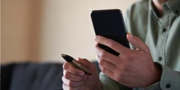 A person sitting on a couch with the mobile and the IQOS VEEV in their hands