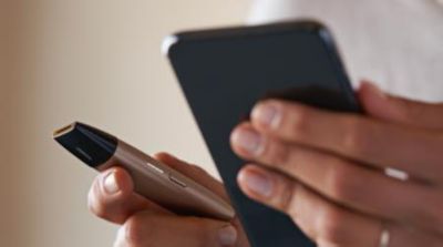A person sitting on a couch with the mobile and the IQOS VEEV in their hands