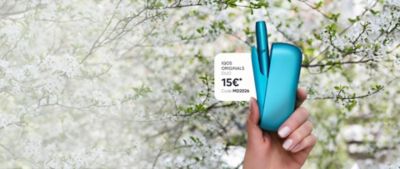 IQOS ORIGINALS Gerät wird von einer Frauenhand vor einem Blütenbaum gehalten