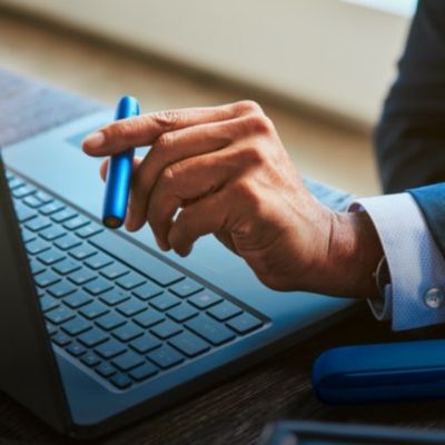 Stellar blue IQOS 3 DUO holder in hand, laptop in background.