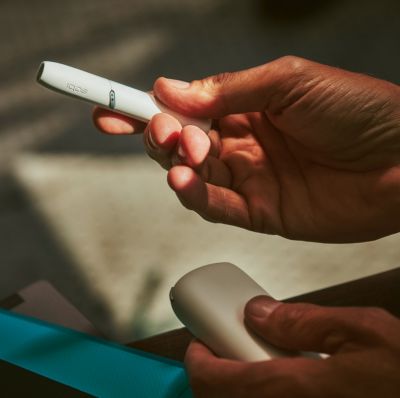 IQOS in white, holder in right hand, charger in left 