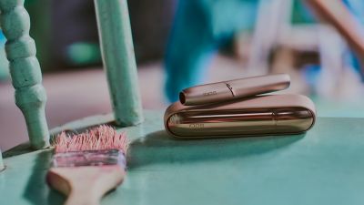 A gold IQOS device on the seat of a woodne chair.