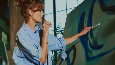 Una artista pintando mientras usa su dispositivo IQOS. 