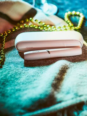 A white IQOS device and holder on a green cloth.