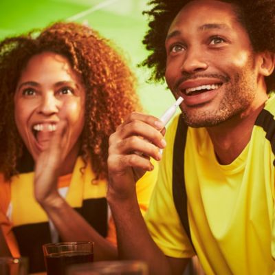 Fans in a sports bar, one using an IQOS device. 