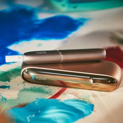 An artist painting while holding an IQOS device.