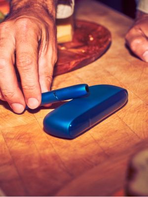 Un hombre sonriente sosteniendo un dispositivo IQOS. 