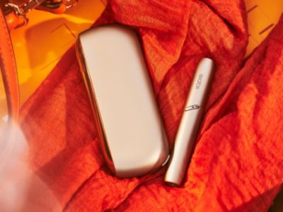 A gold IQOS device and holder on amber-coloured fabric.