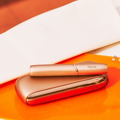 A gold IQOS device and holder on a notepad.