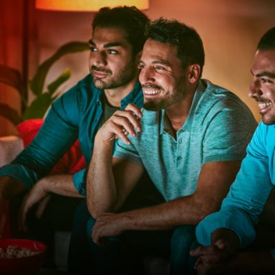 Three men enjoying TV show; one with IQOS holder in hand