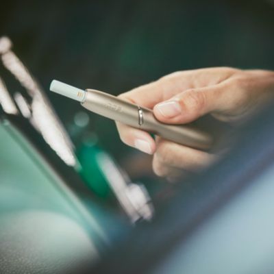 A person's hand, holding an IQOS device.