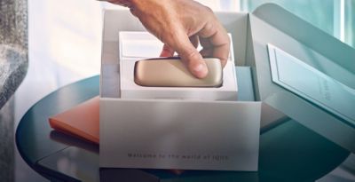 A person removing  a gold IQOS device from its packaging.
