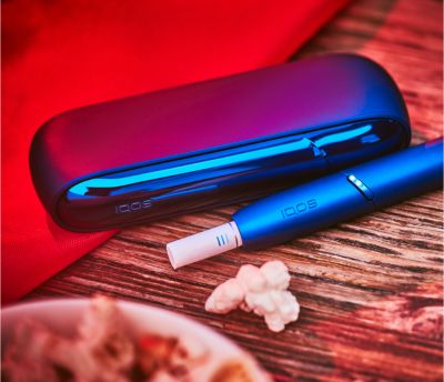 Stellar blue IQOS 3 Duo holder and charger with HEETS stick on a table next to popcorn