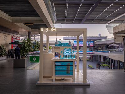Módulo de exhibición IQOS ILUMA en pasillo interior de plaza comercial.
