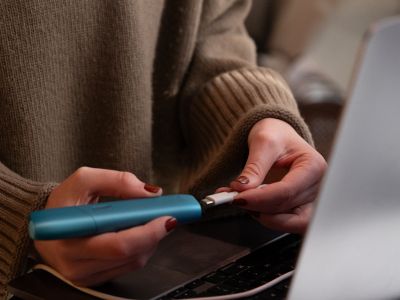 Person verbindet IQOS ORIGINALS ONE Turquoise per USB-Kabel mit Laptop.