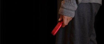 Hand hält IQOS ORIGINALS ONE Scarlet vor dunklem Hintergrund.