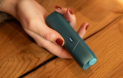 Hand hält IQOS ORIGINALS ONE Turquoise mit leuchtenden LEDs.