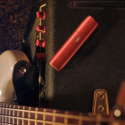 IQOS ORIGINALS ONE Scarlet liegt neben E-Gitarre auf einem Verstärker platziert.