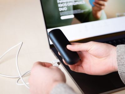 Person verbindet schwarzes IQOS ORIGINALS DUO Gerät per USB-Kabel mit Laptop.
